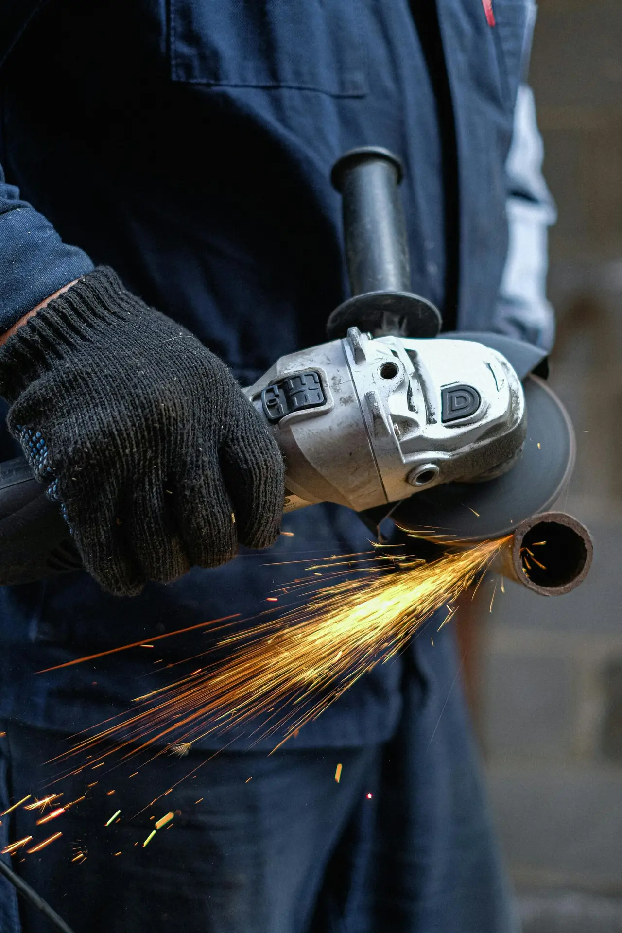 Close-up view of a man using an angle grinder, creating sparks while cutting metal in an indoor workshop.